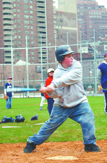 A young baseball player in a helmet and jeans swings a blue bat.