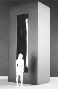 Black and white photo of a person viewing a tall, minimalist sculpture with a glowing vertical line in its center.