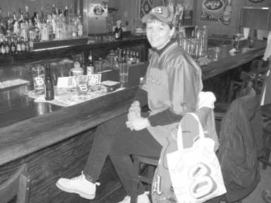 A person sits on a stool at a bar, looking at the camera.
