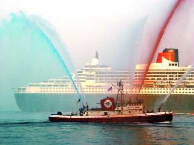 A small tugboat sprays red and blue water in front of a large cruise ship.
