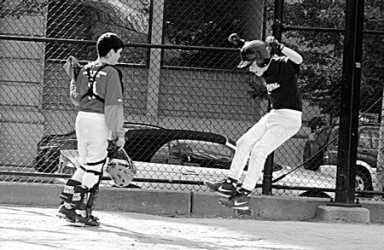 Black and white image of two young baseball players on a field. One is in catcher's gear, and the other appears to be mid-jump or mid-swing.