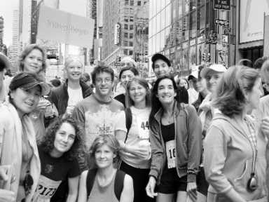Black and white image of a diverse group of people, some wearing race bibs, posing together outdoors.