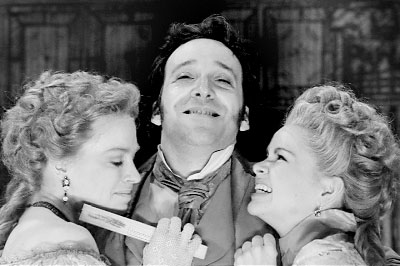 Black and white image of two women in period attire flanking a man with a mustache.