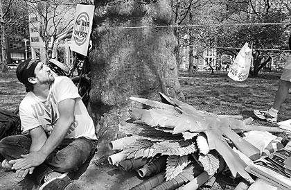 Black and white image of a person sitting near a large tree with debris around its base.