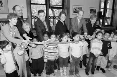 Black and white image of adults and children participating in a ribbon-cutting ceremony indoors.