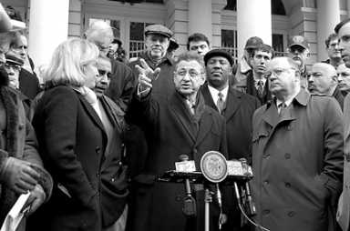 Group of people gathered outdoors, one speaking at a podium.