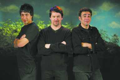 Three men in dark clothing stand with crossed arms against a painted backdrop.