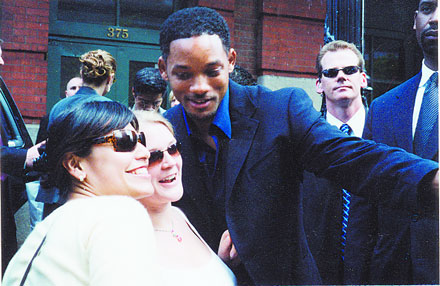 Will Smith taking a selfie with two women, surrounded by other people.