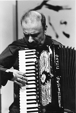 A man with a bald head plays an accordion, looking down at the keys.
