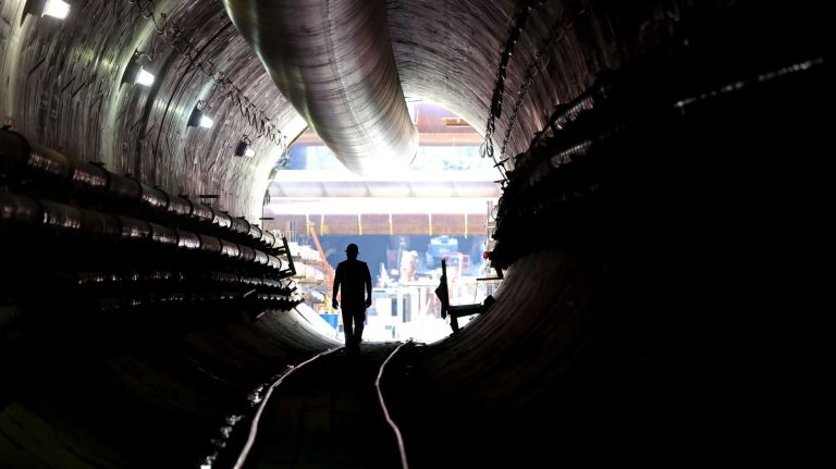 New York, NY - Vince DeNina, Inspector on the East Side Access tunnel project, walks along work tracks of Tunnel B/C in Queens, in the tunnel that now extends to and just 6 feet under the LIRR main tracks in Long Island City with underground tunneling now complete (this is the end where tunneling machines enter, 50 feet below the street). Pipes in the tunnel provide fresh air and others transport fluids and slurry as part of the process. MTA Chairman Joseph Lhota announced that the last drilling machine completed work on July 22 in tunnel B/C as part of the East Side Access project on the Queens side. A TBM drilling/tunneling machine named 