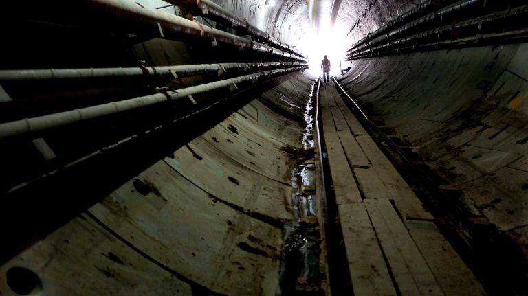 New York, NY - Vince DeNina, Inspector on the East Side Access tunnel project, walks along work tracks of Tunnel B/C in Queens, in the tunnel that now extends to and just 6 feet under the LIRR main tracks in Long Island City with underground tunneling now complete (this is the end where tunneling machines enter, 50 feet below the street). Pipes in the tunnel provide fresh air and others transport fluids and slurry as part of the process. MTA Chairman Joseph Lhota announced that the last drilling machine completed work on July 22 in tunnel B/C as part of the East Side Access project on the Queens side. A TBM drilling/tunneling machine named 