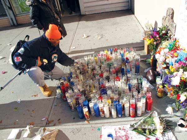 Crying and praying, a man added a candle on Monday to a large memorial for slain Baruch Houses resident Raphael Ward, 16.  Photo by Clayton Patterson