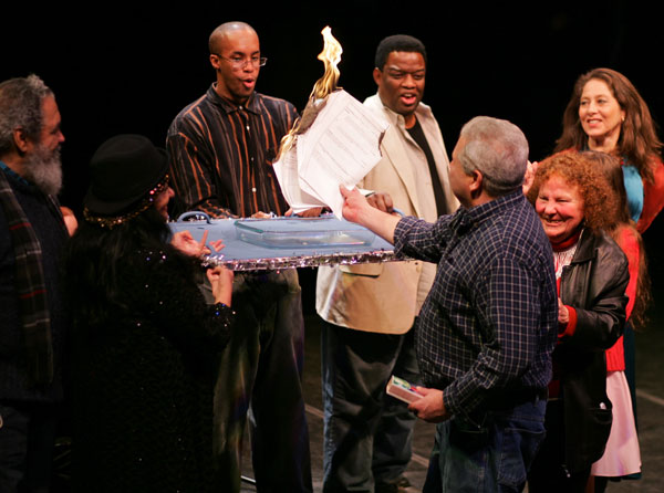 Doing the honors at the burning of Theater for the New City’s mortgage on Jan. 26 were, from left, Chino Garcia, director of CHARAS/El Bohio; Kitty Lunn, a disabled choreographer and artistic director of Infinity Dance Theater (hidden in photo); Bina Sharif, a Pakistani-American playwright; Jerrell Williams, a T.N.C. volunteer; Michael David Gordon, a leading actor with T.N.C. Street Theater; Mark Marcante, T.N.C. actor, writer, composer, set designer and production director; Crystal Field, T.N.C. executive artistic director; Briana Bartenieff, a young T.N.C. actress (hidden behind Fields); and Elizabeth Ruf, community activist, theater artist and De Colores Garden co-founder.  Photo by Sam Spokony