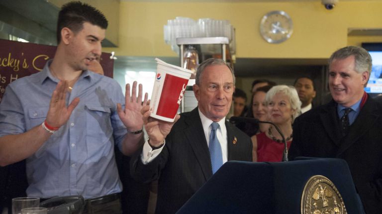 Greg Anagnostopoulos, right, the owner of Lucky's Restaurant reacts as Mayor Michael Bloomberg holds a 64-ounce beverage container during a press conference to discuss local businesses support of the sugary beverage ban. (March 12, 2013)
