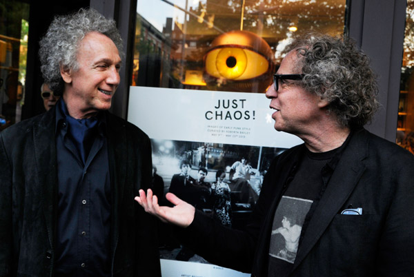 Bob Gruen, left, and Godlis, who documented the punk scene with their photography, caught up at the opening. The image on the “Just Chaos” show poster/invite, behind them, was a shot by Godlis.