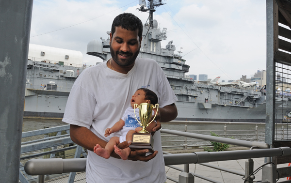 Aaron Singh, captain of the Seaport Museum's Decker, holding his six-week-old son, Theodore, and a trophy won by the tug. Downtown Express photo by Terese Loeb Kreuzer)