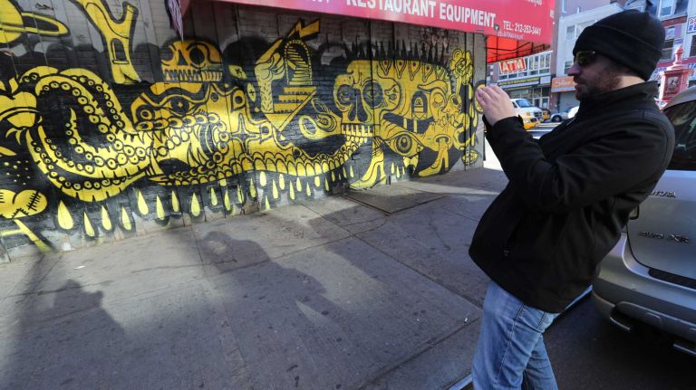 Amir Raanan (visiting from Israel) photographs artwork on the wall of a building at Rivington Street and the Bowery durning a Graf Tours visit to the Lower East Side. ( Nov. 24, 2013)