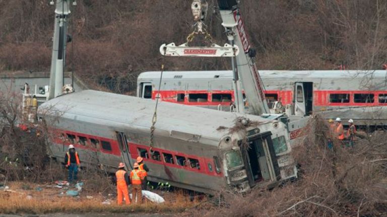 Workers upright and move a derailed Metro-North train car in the Bronx.