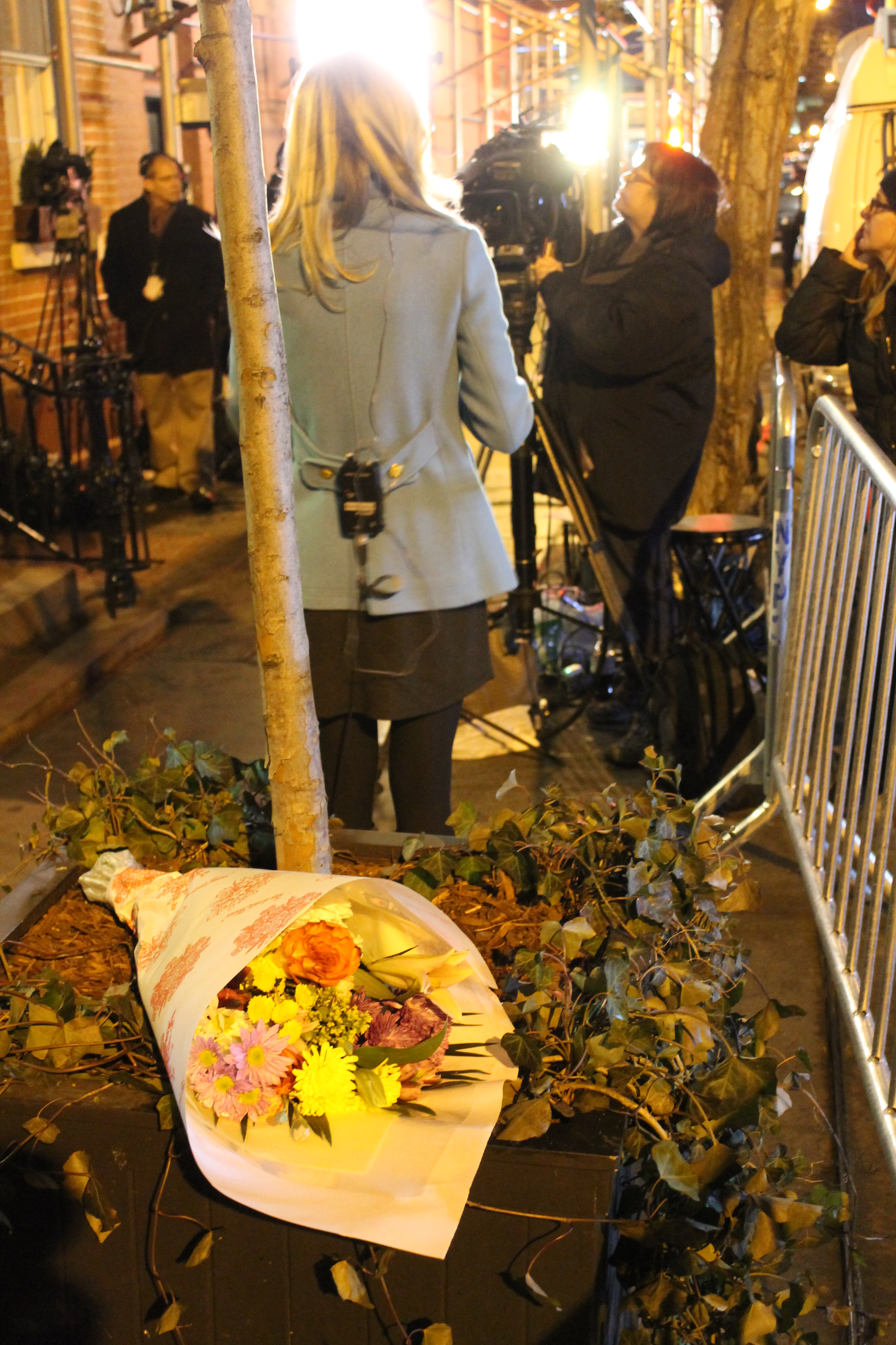Someone had left flowers for Hoffman outside his building, as a TV news reporter prepared to do her on-the-scene "stand up."  Photo by Lincoln Anderson