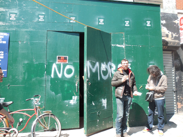 Two men working on the new Nublu space outside the site this week. Someone had written “NO MORE BARS” on the construction fence, which was later altered to read simply “NO MORE.”  PHOTO BY GERARD FLYNN