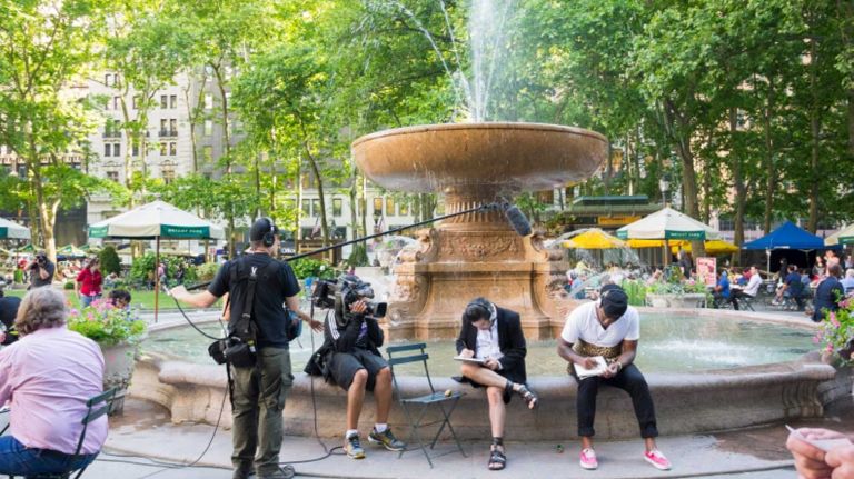 A crew films contestants during a Project Runway Allstars shoot by the fountain in Bryant Park in Manhattan. Many park goers can be seen. Project Runway is a competition based reality show for aspiring fashion designers. Project Runway Allstars is a spinoff where contestants are drawn from previous Project Runway seasons. 