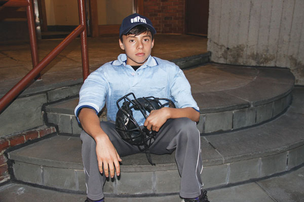 Cameron Schneider — posing for a photo on a weekday while wearing his ump’s uniform and chest protector outside his West Village home — is part of a new generation learning the art of umpiring at Greenwich Village Little League.  PHOTO BY TEQUILA MINSKY