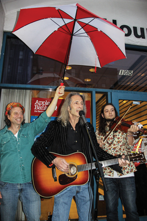 Phil Hartman, of Two Boots Pizza, a co-sponsor of the plaque initiative, held the umbrella as Lenny Kaye performed “Uncle John’s Band” at the Fillmore East plaque unveiling.