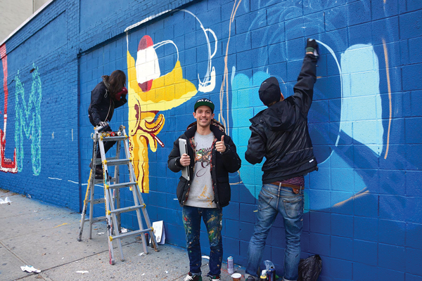 Greg Edgell of the arts group Green Villain standing in front of the new “Alphabet City” mural that he and collaborators The Yok and Sheryo are creating on the RCN building at Avenue C and E. Sixth St. RCN chose their mural over one pitched by Loisaida street artist Chico.  Photo by Sarah Ferguson