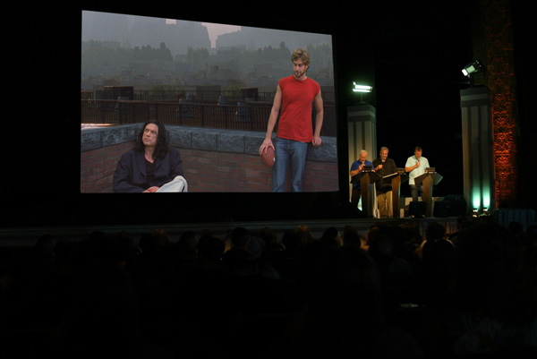 Two Cults, One Night: RiffTrax Lampoons ‘The Room’ 2 L to R: Bill Corbett, Kevin Murphy and Michael J. Nelson riff “The Room.” Pictured onscreen, L to R: Tommy Wiseau as Johnny, Greg Sestero as Mark. Courtesy of RiffTrax