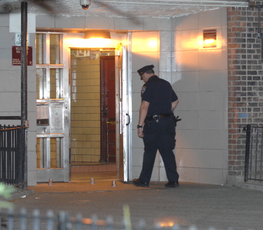 A police officer in the doorway at 178 Avenue D on Wednesday night after a shooting had occurred there around 11 p.m. Three cups are placed on the ground over spots where spent bullet casings were recovered.  Photos by C4