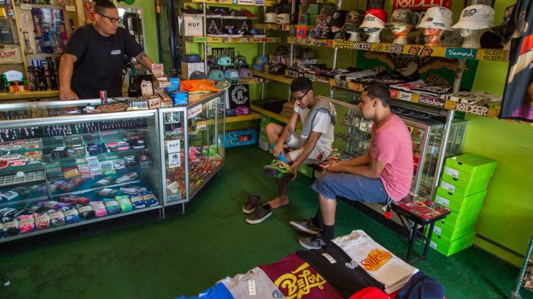 Employee Kevin Gutierrez (left) looks on as customers Kevin Gonzalez and Joshua Reyes (right) try on shoes in Sideshow in Middle Village on July 12, 2015.