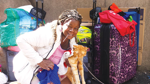 Diane Majett, clamping one of her knitting needles in her teeth while holding up Buttercup, who models Majett’s hand-knit cat coats.   Photo by Lincoln Anderson