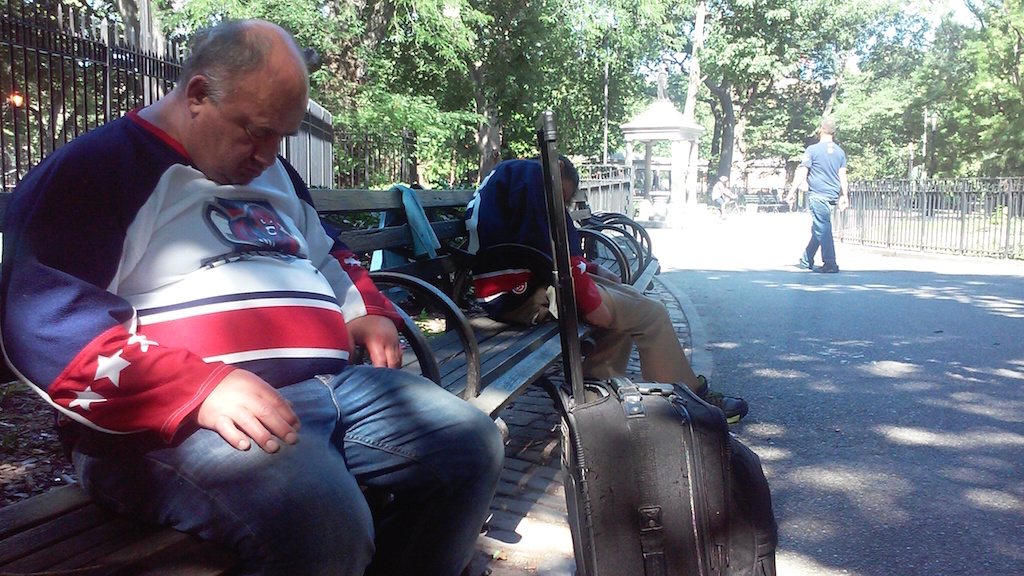 A man dozes in a sitting position with his luggage nearby.
