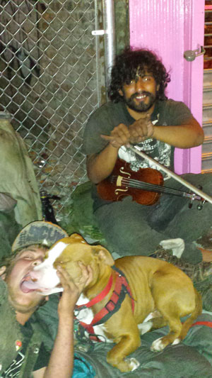 Cole, left, kissing his pit bull, Riley, with fiddle player Anthony in the background. Photo by Lincoln Anderson