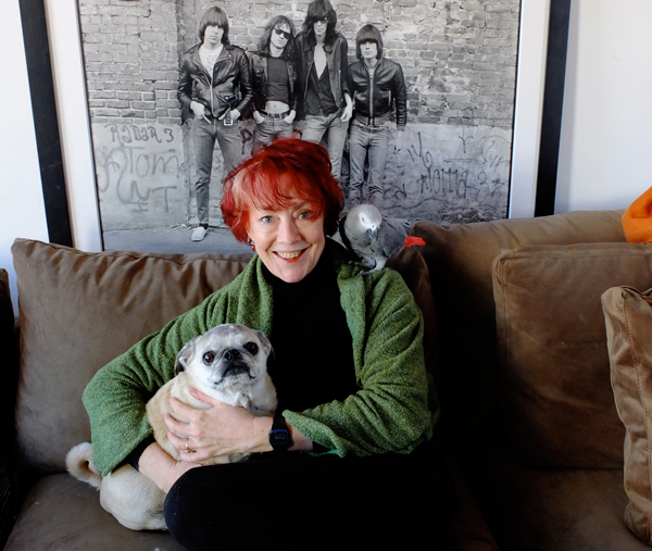 Roberta Bayley with Sidney, her pug, in 2013 in a photo for an article in The Villager about the Washington Square Park dog run calendar. She allowed her classic photo of the Ramones, behind her, to be used for the calendar’s cover, except with the band members’ heads replaced with the heads of four pugs from the run.  Photo by Godlis