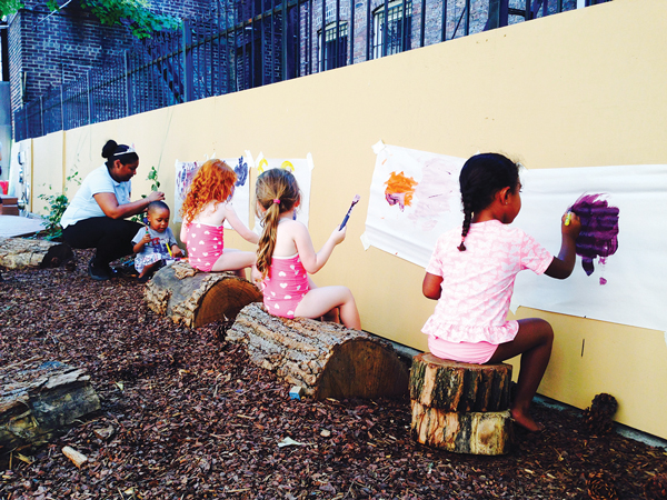 Tykes log some time painting in Elements Preschool’s nature-based backyard.