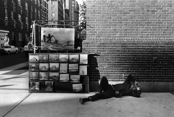 “Surf ’n Turf” (1979) captures the irony of an apparently homeless man sleeping on a Manhattan sidewalk next to paintings of crashing ocean surf and quiet country landscapes. Courtesy Steven Kasher Gallery, New York.