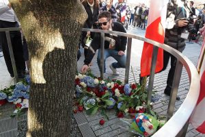 Photo by Milo Hess Locals place tricolor bouquets at the memorial’s famed “Survivor Tree.”