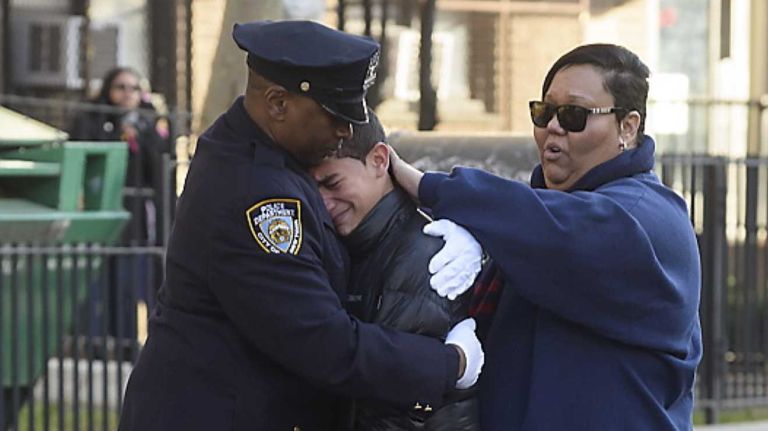 Jade Ramos, center, hugs a New York Police Department officer after a prayer and wreath laying ceremony for his father, Detective Rafael Ramos, and Detective WenJian Liu on Tompkins Avenue in Brooklyn on Sunday, Dec. 20, 2015. Liu and Ramos were shot and while in a squad car on Tompkins Avenue last December.