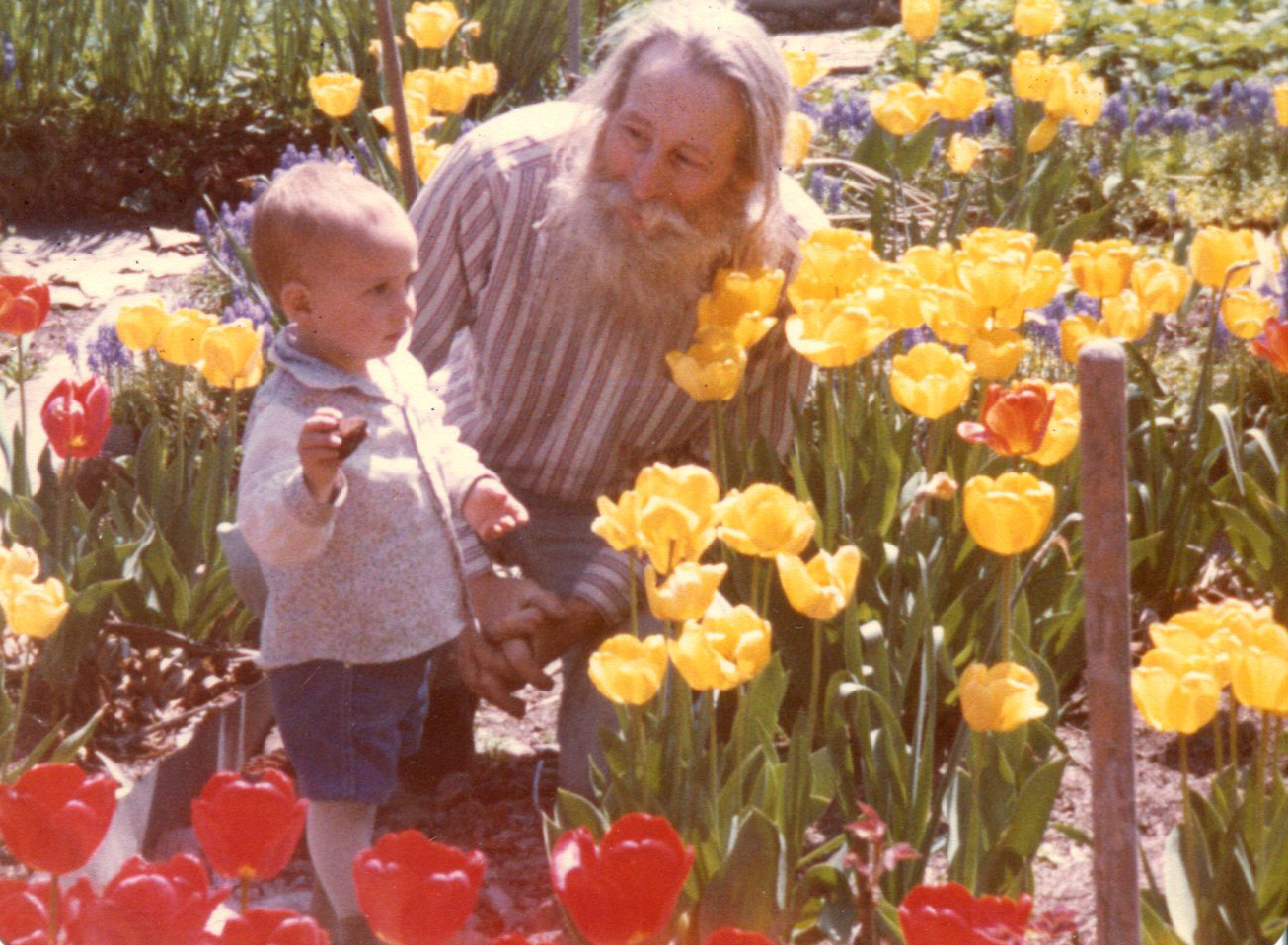 Adam Purple, a new father again at age 52, in April 1982 with his only son, also named Adam, almost age 2, amid a riot of tulips in the Garden of Eden on Forsyth St.