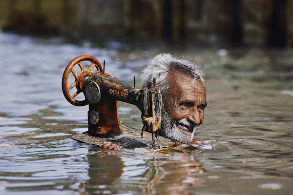 Steve McCurry sees India, in spectacular color 4 “Tailor Carries His Sewing Machine through Monsoon Waters, Porbandar, Gujarat, 1983.” Photo © Steve McCurry.