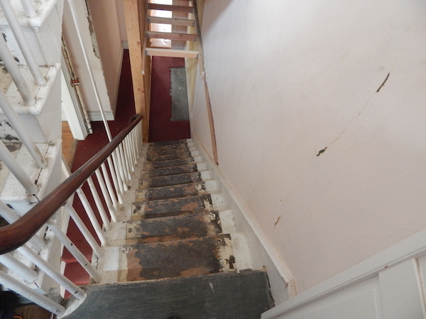 An inside view of the house shows sloped stairs, a cracked wall, and wood reinforcements placed by the current owner after DOB violations were issues. Photo by Sean Egan.