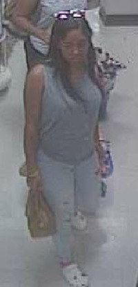 The first suspect, last seen wearing a gray shirt, light blue jeans, and white sandals, with sunglasses on top of her head, carrying a bag. Courtesy DCPI.