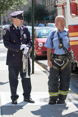 The “Taps” player speaks with a Fire Officer while waiting for the procession to reach the corner of W. 19th St. & Seventh Ave. Photo by Daniel Kwak.