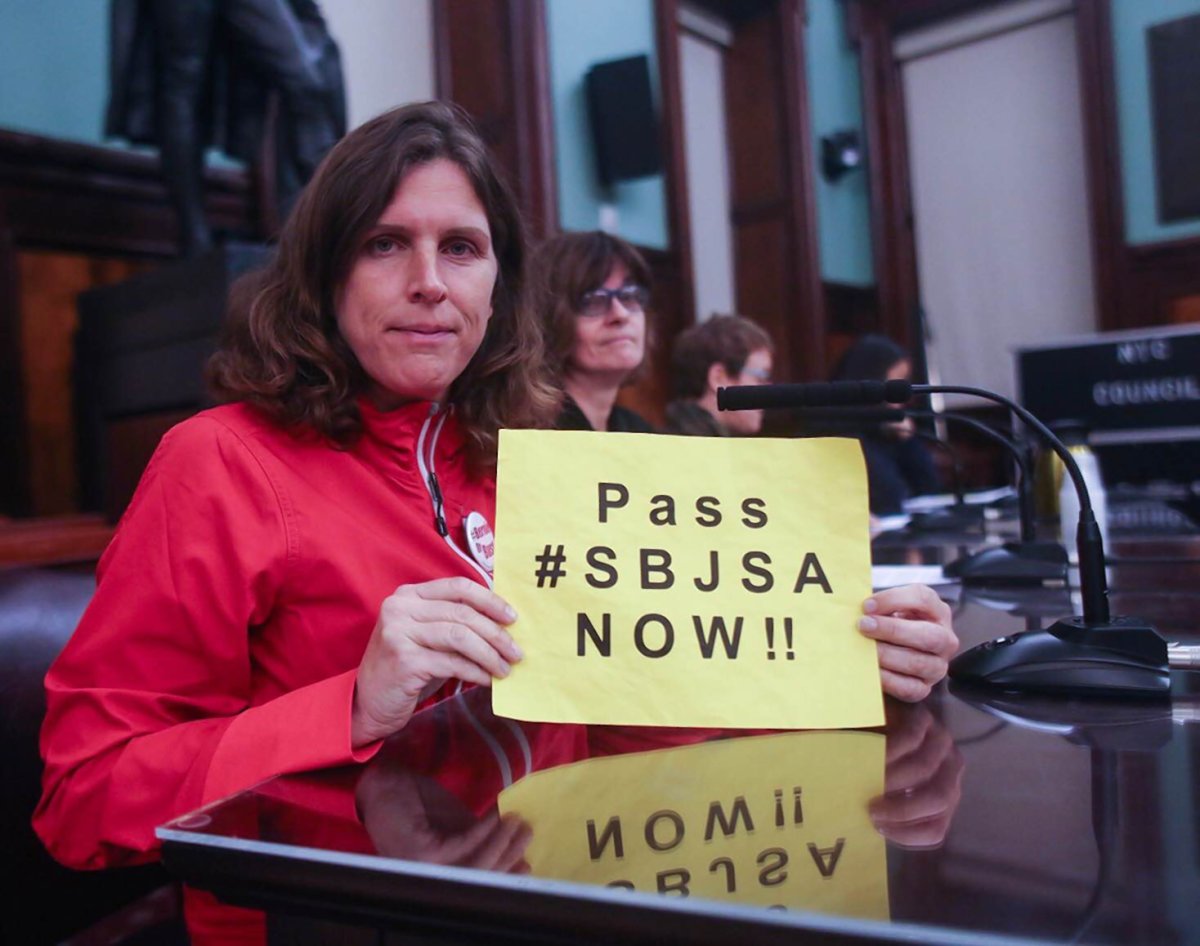 At last week’s City Hall hearing on small business, Emily McCoy, a Tribeca resident who formerly had a small store on Duane St., held up a sign in support of the Small Business Jobs Survival Act. However, once again, the long-stalled measure was not on the committee’s agenda.  Photo by William Alatriste / NYC Council