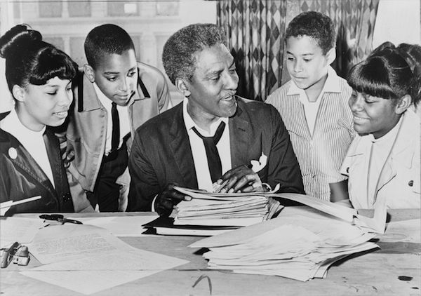 Bayard Rustin (center) speaking with (left to right) Carolyn Carter, Cecil Carter, Kurt Levister and Kathy Ross, before a 1964 demonstration. Photo: World Telegram & Sun photo by Ed Ford via Wikimedia.