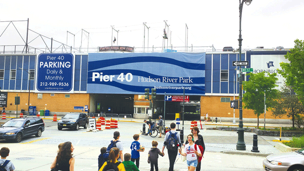 A typical scene at Pier 40 in Hudson River Park includes droves of young athletes and parents streaming to and from the pier’s artificial-turf sports fields. The trapeze seen at the top of the photo has relocated to Williamsburg. The Hudson River Park Trust and local youth sports leagues will be looking at ideas for removing all or parts of the pier shed on the east (above) and west sides of the pier, and re-massing the pier’s commercial space on its northern and southern edges. If that is done, then in the future, the above view might show the pier’s playing fields with the Hudson River and sky visible in the background. Photo courtesy The Villager.