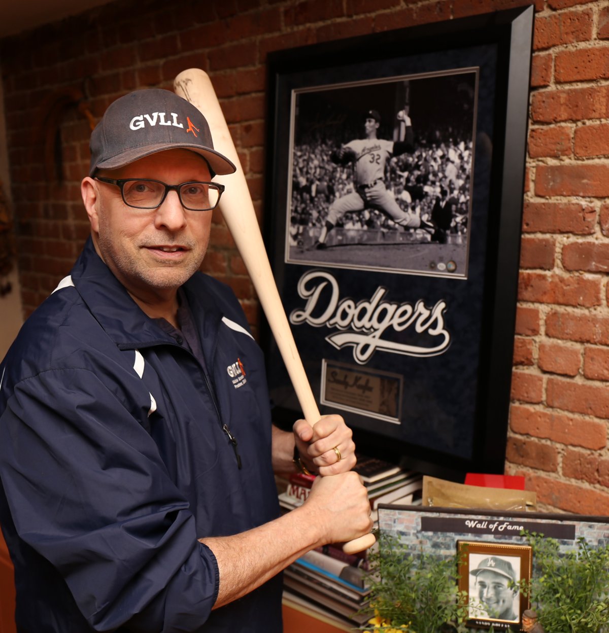 Ready to take his swings: New G.V.L.L. President Michael Schneider in front of a photo of one of his idols, Sandy Koufax, the legendary lefty. Schneider’s e-mail address has “koufax” in it and his poodle is named Koufax, too. Photo by Tequila Minsky