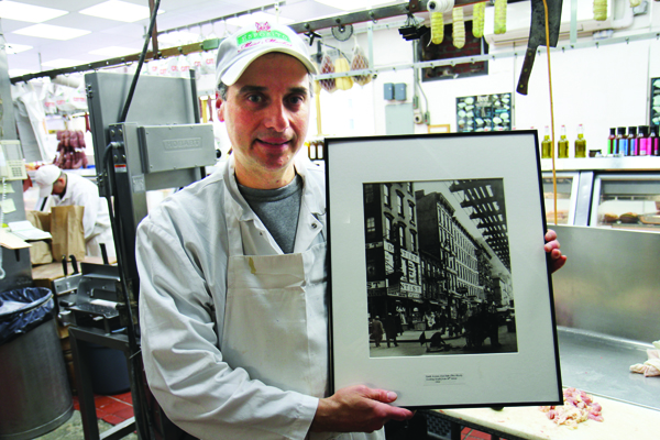 Third-generation owner Robert Esposito holds up a photo of the block from 1932, the year his grandfather Giovanni opened the butcher shop, then one of many in the area once known as Paddy’s Market. | DENNIS LYNCH 