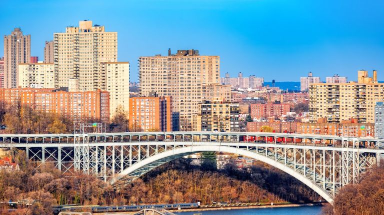 Henry Hudson Bridge spans Spuyten Duyvel Creek, in New York City. Harlem apartment buildings shine under the late afternoon light.